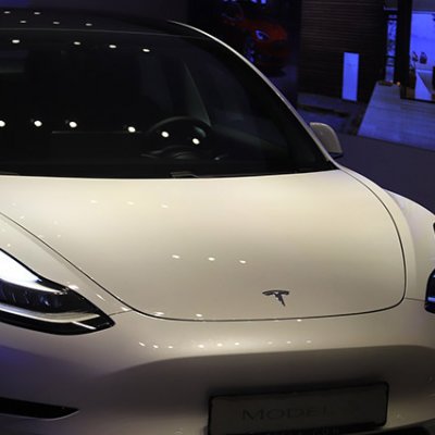 A futuristic Tesla car sits in a showroom with blue lights in the background